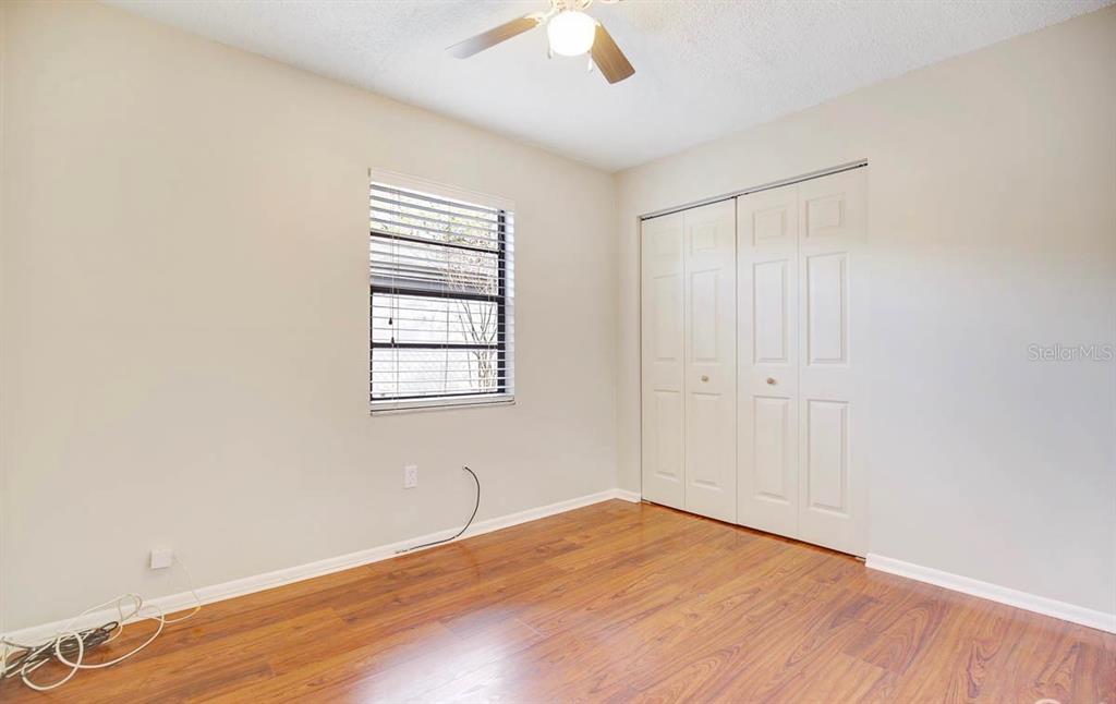 An empty bedroom features light-colored walls, wood-look flooring, a window with blinds, and closet doors — 6319 S CHURCH AVENUE, TAMPA, FL
