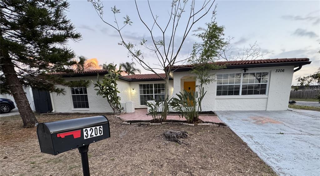 A single-story house with a white stucco exterior, red tile roof, and a yellow door — 3206 PINON DRIVE, HOLIDAY, FL