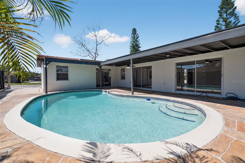 A backyard swimming pool sits on a stone patio next to a white house — 3206 PINON DRIVE, HOLIDAY, FL