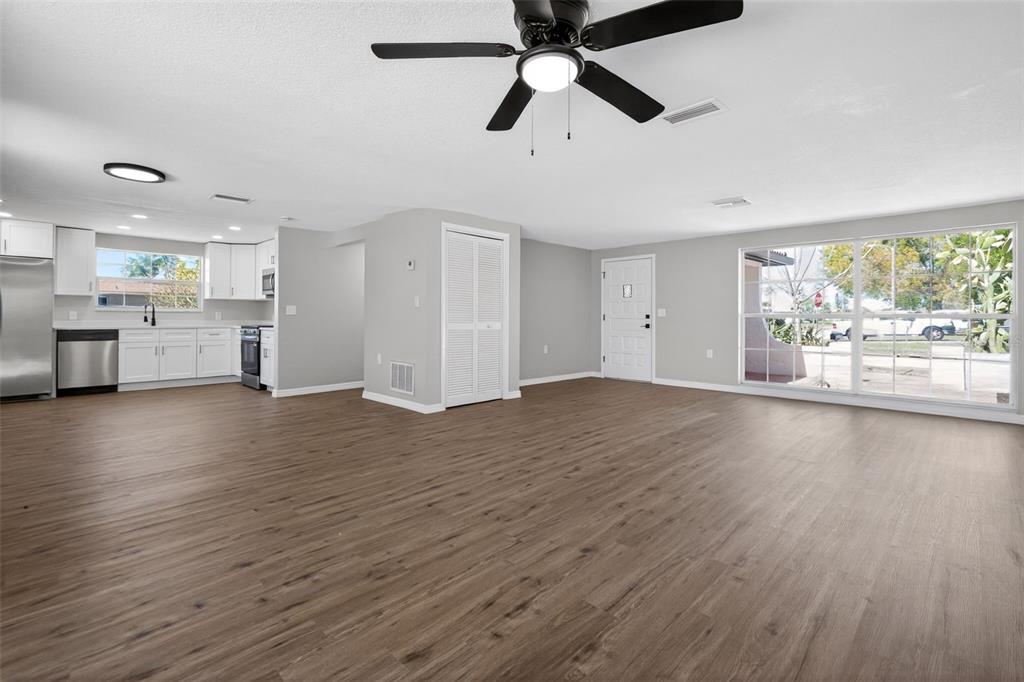 An open-concept living area with wood-look flooring, a ceiling fan, and an adjacent white kitchen — 3206 PINON DRIVE, HOLIDAY, FL