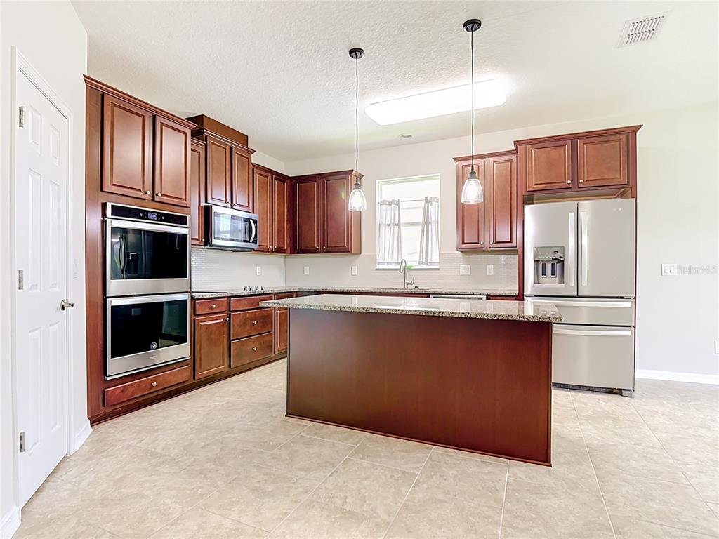 A kitchen with dark wood cabinets, stainless steel appliances, granite countertops, and a central island — 2687 GASPIRILLA CIRCLE, KISSIMMEE, FL