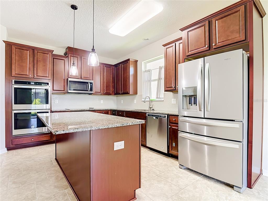 A kitchen features dark wood cabinets, granite countertops, stainless steel appliances, and a center island — 2687 GASPIRILLA CIRCLE, KISSIMMEE, FL