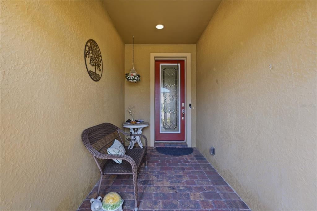 A covered entryway features a red front door, a wicker bench, and brick flooring — 13920 KARINA STREET, VENICE, FL