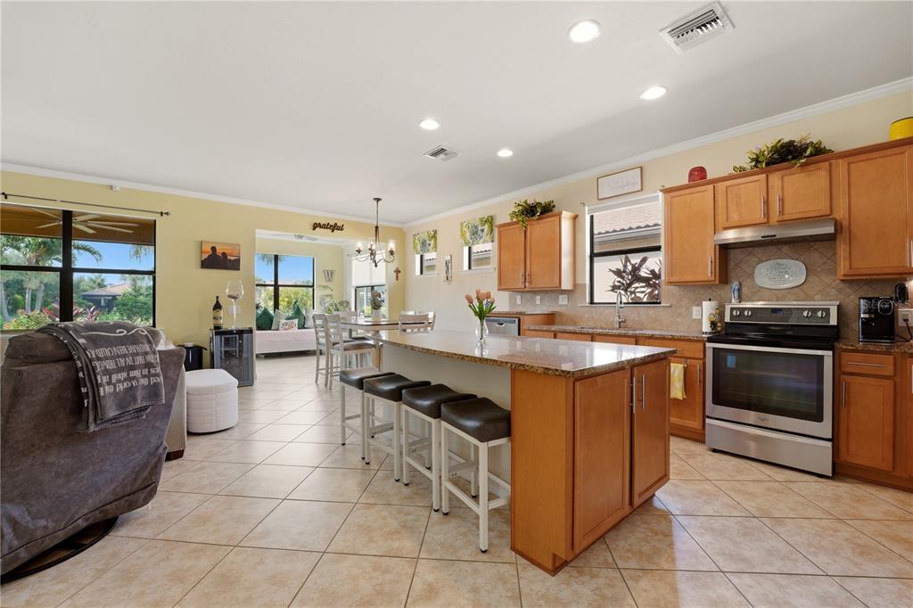 A kitchen with wood cabinets, a granite island, and tile flooring opens to a dining area — 13920 KARINA STREET, VENICE, FL