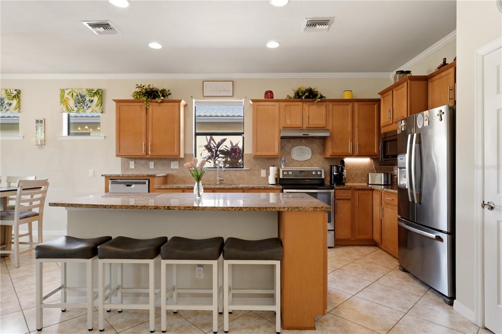 A kitchen features wood cabinets, granite countertops, a center island with bar seating, and appliances — 13920 KARINA STREET, VENICE, FL