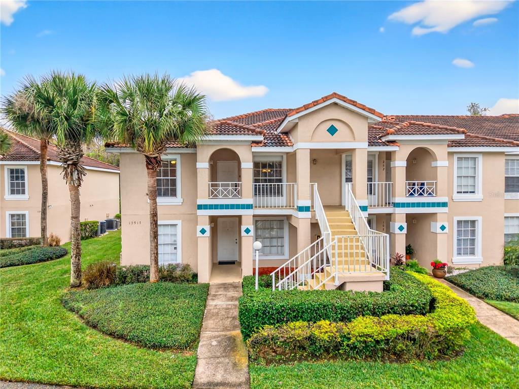 A two-story tan stucco apartment building with a central staircase and palm trees — 13917 TIMBERLAND DRIVE UNIT 201, ORLANDO, FL