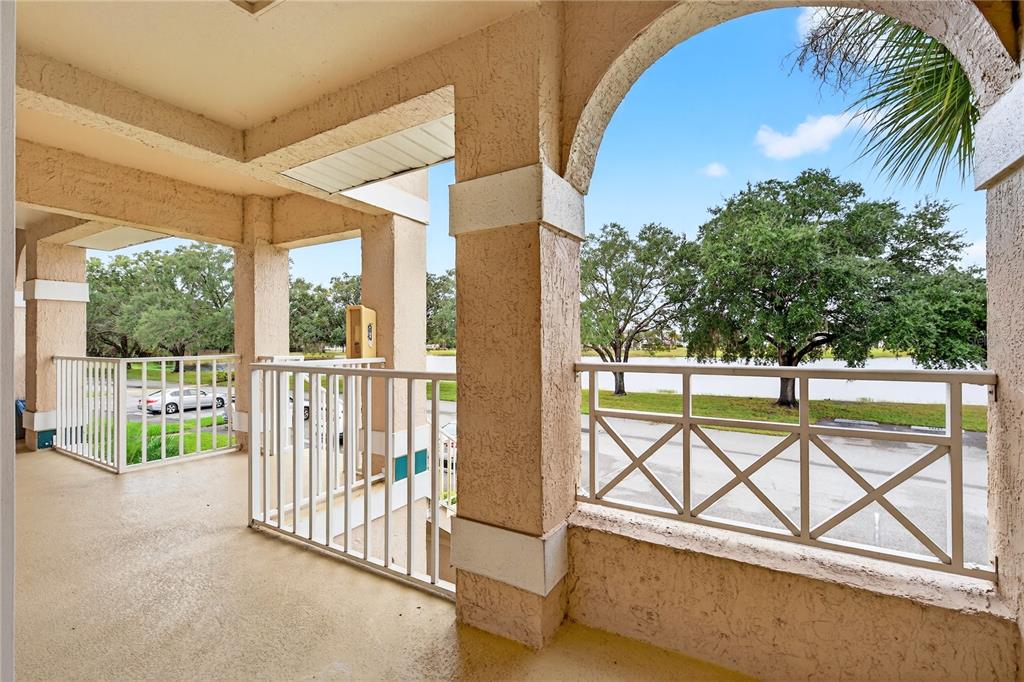 A covered balcony with beige stucco columns, white railings, and a view of trees and water — 13917 TIMBERLAND DRIVE UNIT 201, ORLANDO, FL