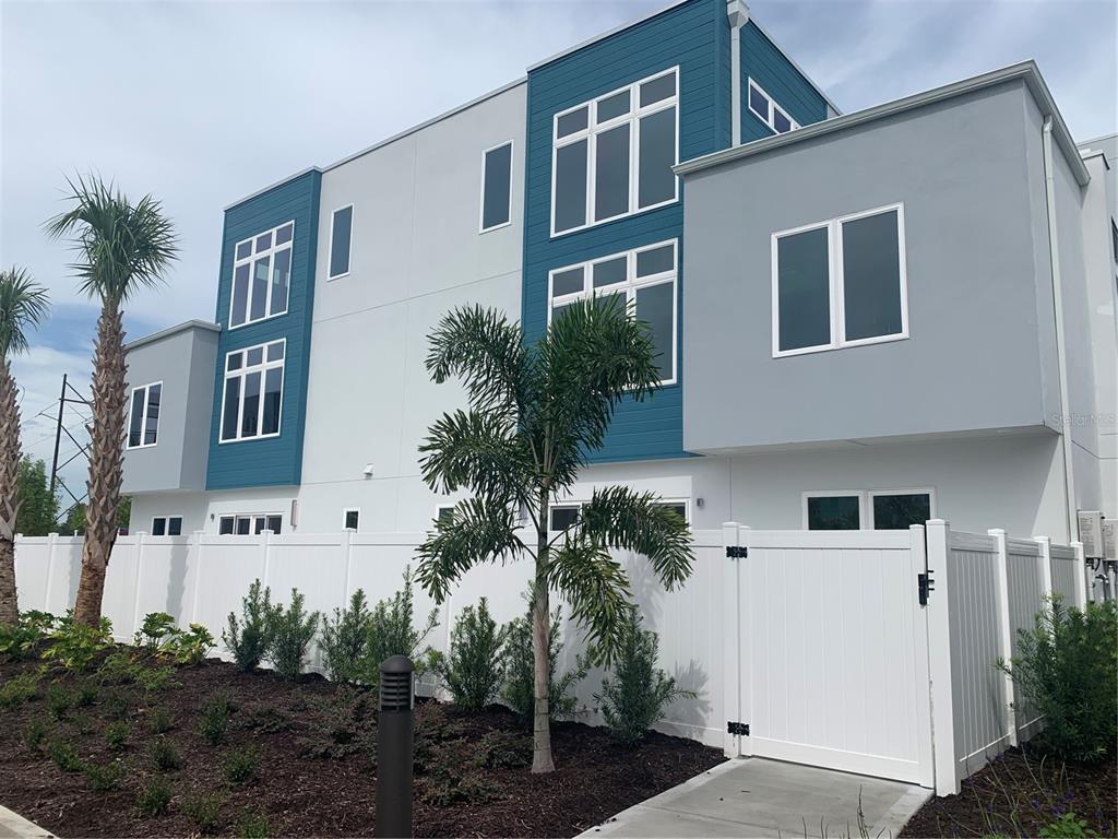 A modern multi-story townhouse exterior with blue siding, gray walls, and a white privacy fence — 7770 SANDY RIDGE DRIVE UNIT 210, REUNION, FL