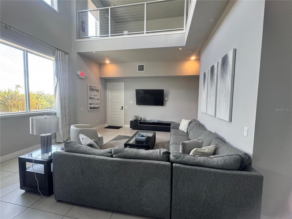 A living room features a high ceiling, a gray sectional sofa, and a loft balcony — 7770 SANDY RIDGE DRIVE UNIT 210, REUNION, FL