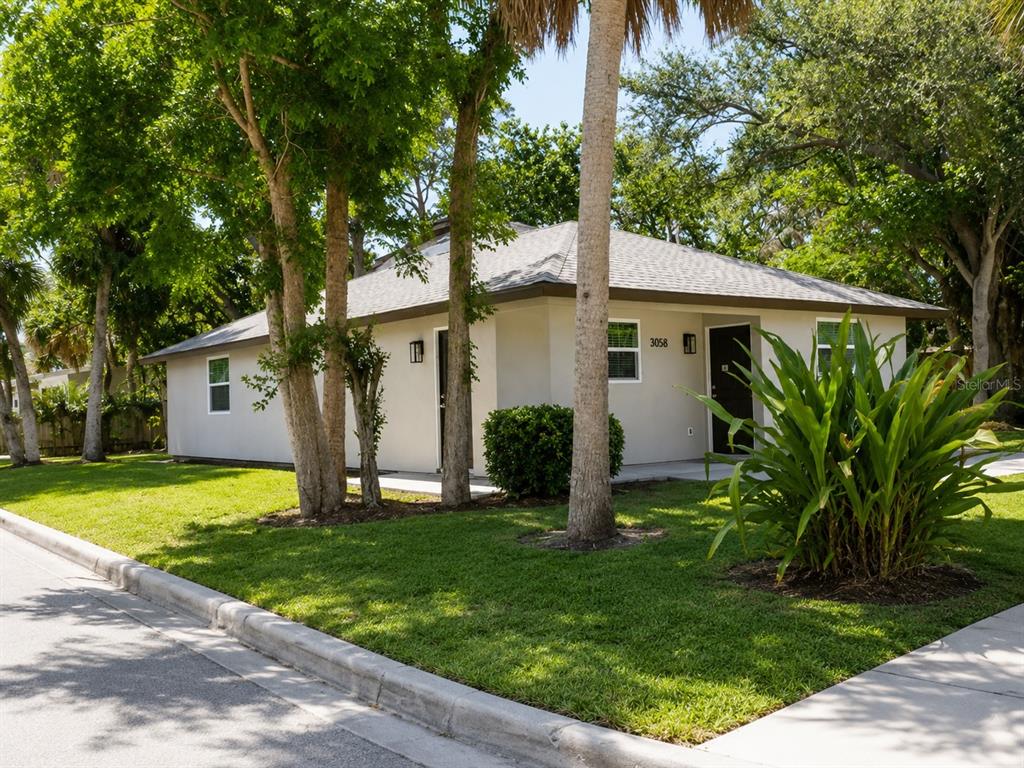 A single-story house with a light-colored exterior, a gray roof, and surrounding trees and lawn — 3058 PALMADELIA AVENUE, SARASOTA, FL