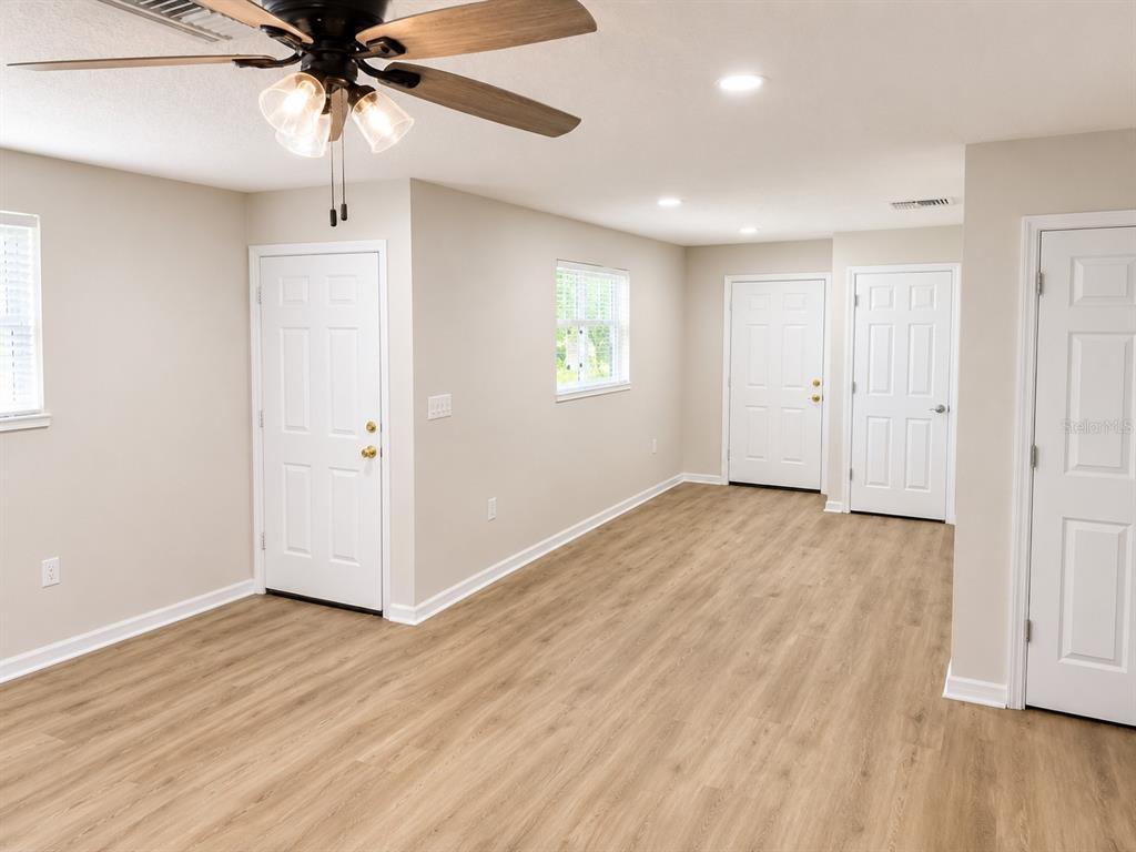 An interior room with light wood-look flooring, beige walls, a ceiling fan, and three white doors — 3058 PALMADELIA AVENUE, SARASOTA, FL