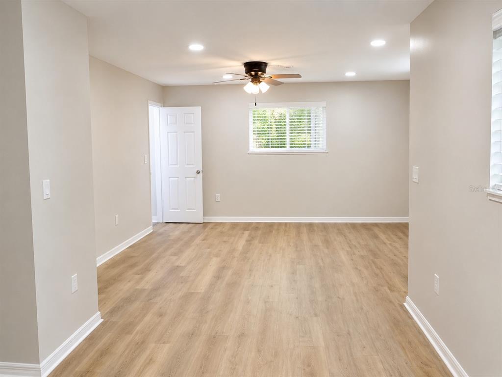 An empty room features light wood-look flooring, beige walls, a ceiling fan, and a window — 3058 PALMADELIA AVENUE, SARASOTA, FL