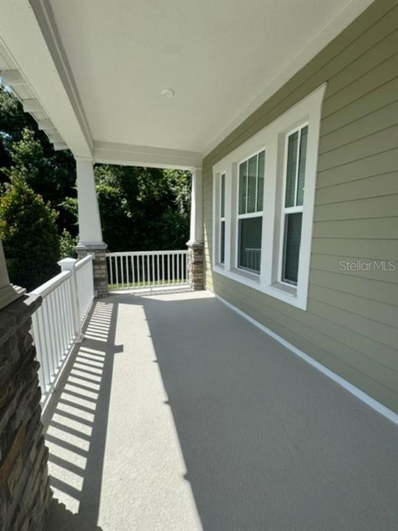 A covered porch with light-colored flooring, white railings, and sage green siding on the house — 7573 ESTUARY LAKE LOOP, CELEBRATION, FL