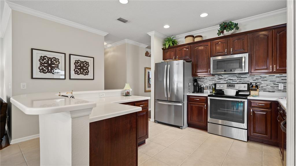 A kitchen features dark wood cabinets, stainless steel appliances, and a white breakfast bar counter — 13560 HAWK LAKE DRIVE, ORLANDO, FL