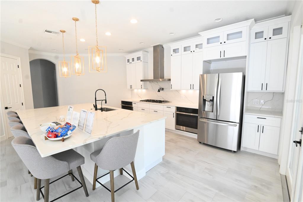 A modern kitchen features white cabinetry, a large marble-topped island, and stainless steel appliances — 6119 FOXFIELD COURT, WINDERMERE, FL