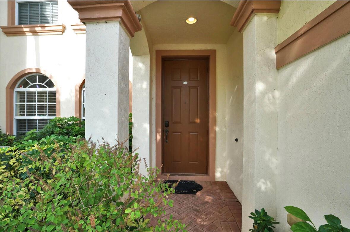 A brown front door sits under a covered entryway with white columns and brick flooring — 16097 Poppyseed Circle # 1905, Delray Beach FL 33484, DELRAY BEACH, FL