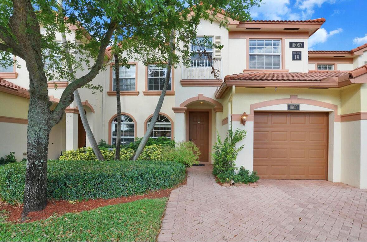 A two-story townhouse exterior features a brown garage door, a paved driveway, and landscaping — 16097 Poppyseed Circle # 1905, Delray Beach FL 33484, DELRAY BEACH, FL