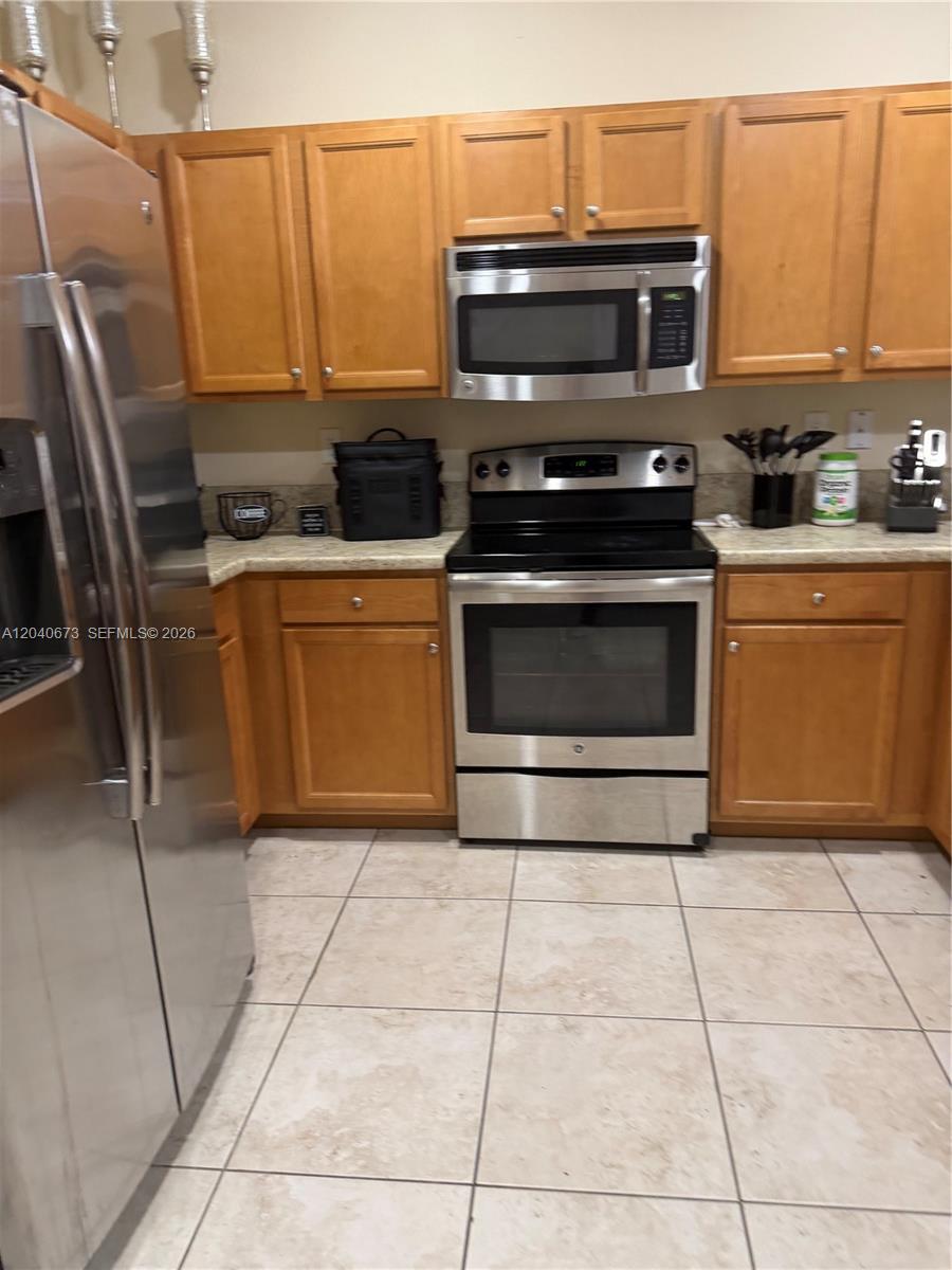 A kitchen features light wood cabinets, stainless steel appliances, and beige tile flooring — 8929 W 35th Way, Hialeah FL 33018, HIALEAH, FL