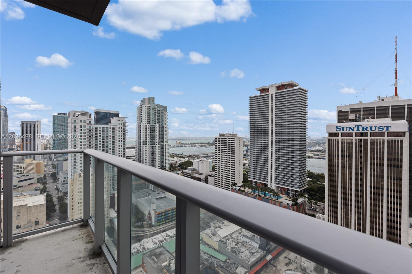 A high-rise balcony overlooks a dense urban skyline with several skyscrapers and a distant bay — 151 SE 1st St # 3202, Miami FL 33131, MIAMI, FL