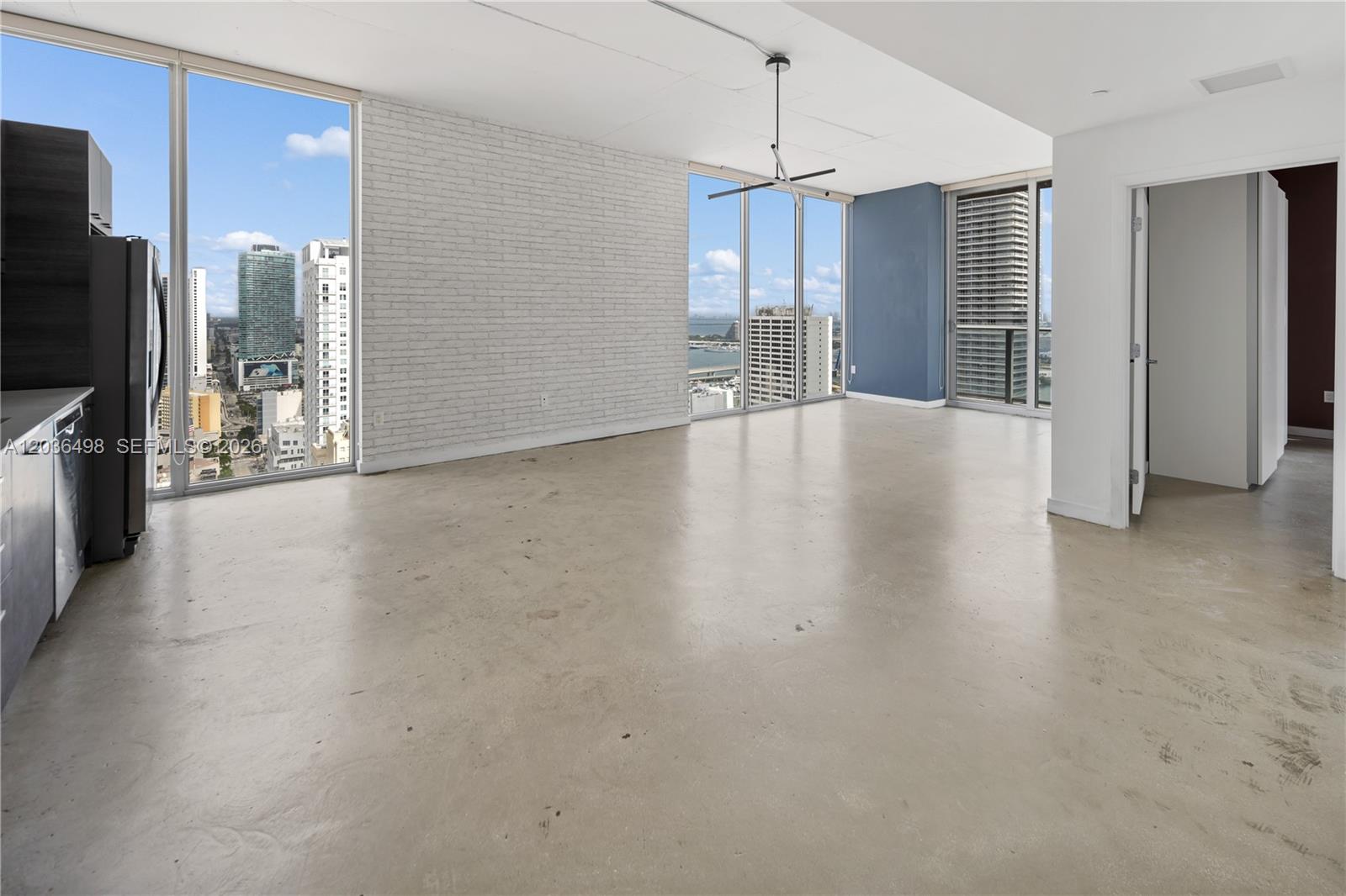 An open-concept living area features concrete floors, a white brick wall, and floor-to-ceiling windows — 151 SE 1st St # 3202, Miami FL 33131, MIAMI, FL