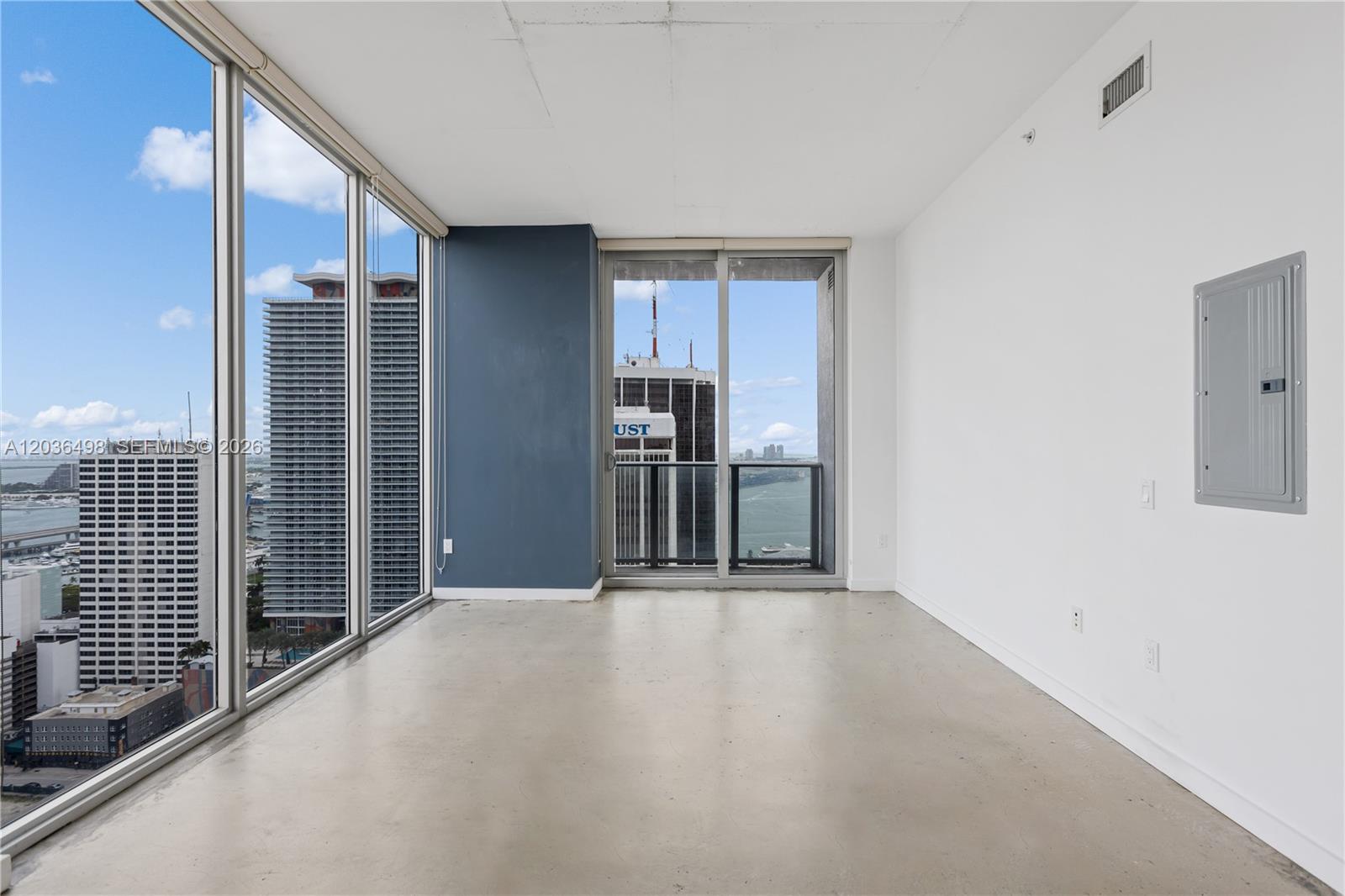 An empty room features floor-to-ceiling windows, concrete flooring, a blue accent wall, and city views — 151 SE 1st St # 3202, Miami FL 33131, MIAMI, FL