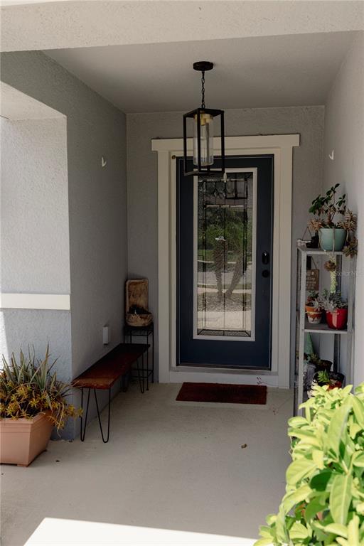 A covered front porch features a dark blue door, a wooden bench, and potted plants — 1630 SCARBROUGH ABBY PLACE, ST CLOUD, FL