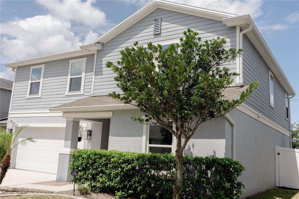 A two-story house with light gray siding, a garage, and a large bush in front — 1630 SCARBROUGH ABBY PLACE, ST CLOUD, FL