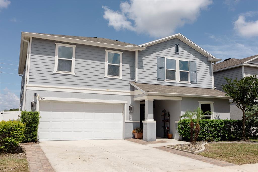 A two-story house with light gray siding, a white garage door, and a covered entryway — 1630 SCARBROUGH ABBY PLACE, ST CLOUD, FL
