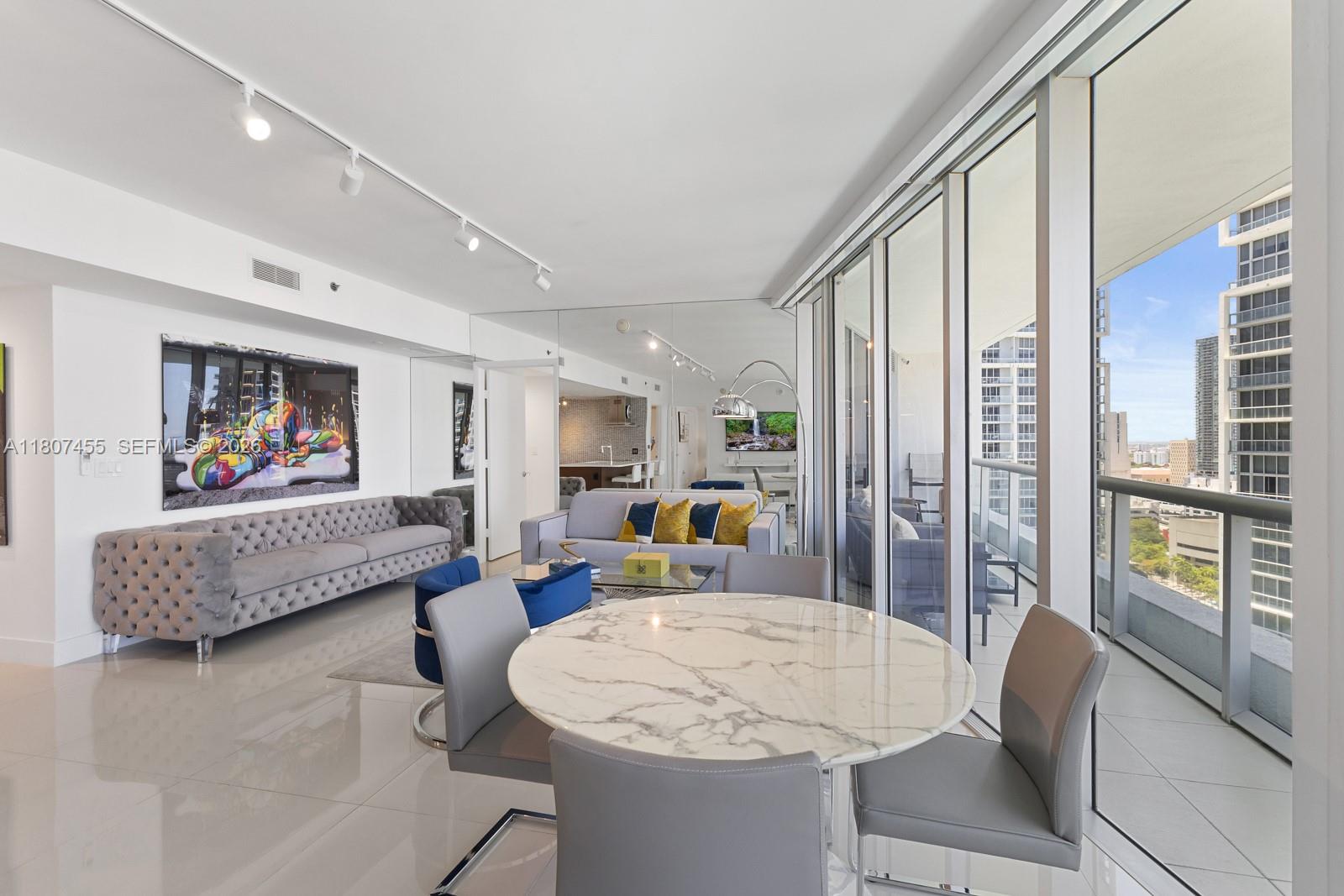 A modern living and dining area features a marble table, grey sofa, and floor-to-ceiling windows — 495 Brickell Ave # 2304, Miami FL 33131, MIAMI, FL