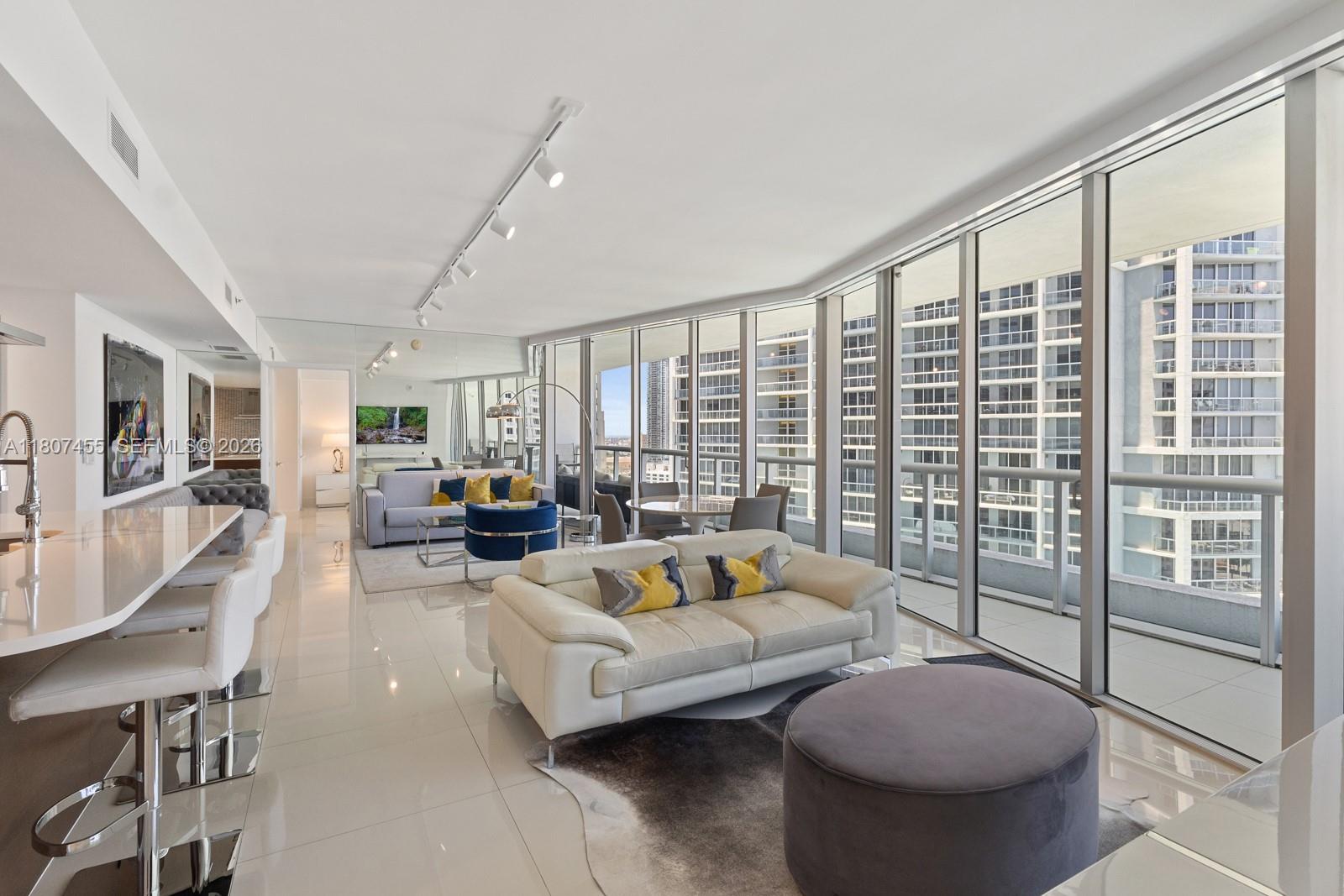 A modern living room with white tile floors, a white sofa, and floor-to-ceiling windows — 495 Brickell Ave # 2304, Miami FL 33131, MIAMI, FL