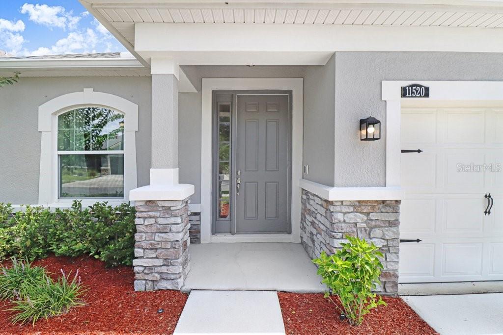 The exterior of a house features a gray front door, stone accents, and a garage — 11520 BLUE WOODS DRIVE, RIVERVIEW, FL