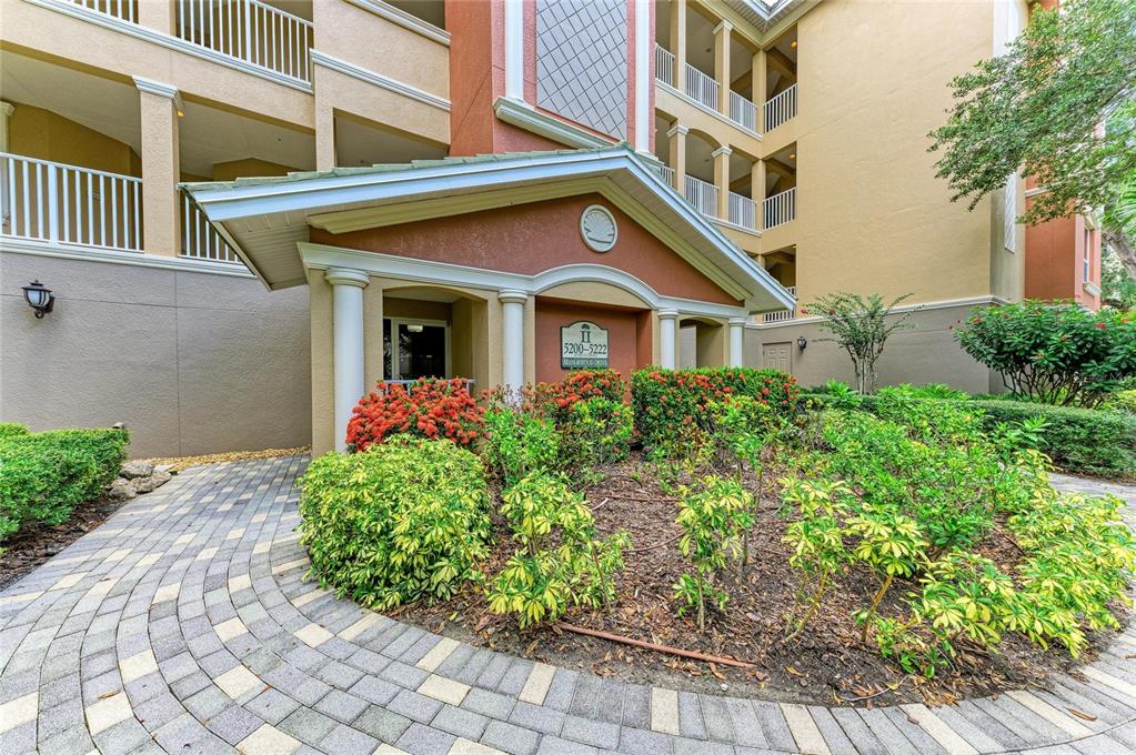 A paved walkway leads to the entrance of a multi-story apartment building with landscaping — 5200 MANORWOOD DRIVE UNIT 2D, SARASOTA, FL
