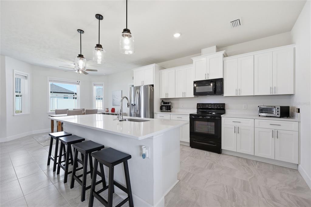 A bright kitchen features white cabinetry, a quartz island with bar seating, and black appliances — 2168 SW 245TH DRIVE, NEWBERRY, FL