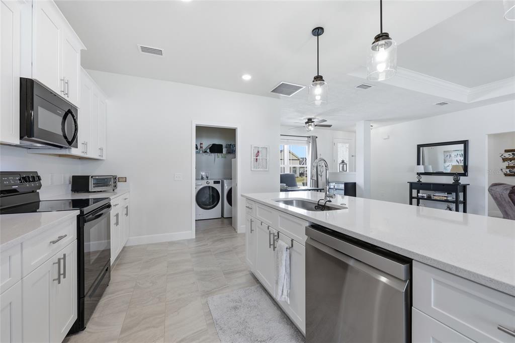 A modern kitchen features white cabinets, quartz countertops, stainless steel appliances, and a laundry room — 2168 SW 245TH DRIVE, NEWBERRY, FL