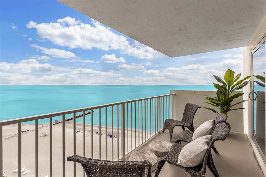 A balcony with wicker furniture overlooks a sandy beach and the turquoise ocean — 2301 GULF OF MEXICO DRIVE UNIT 102N, LONGBOAT KEY, FL