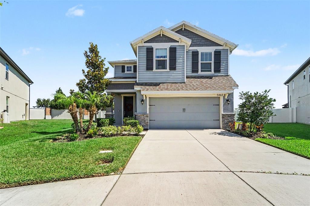 A two-story suburban house features a gray garage, light blue siding, and a concrete driveway — 5463 LITTLE STREAM LANE, WESLEY CHAPEL, FL