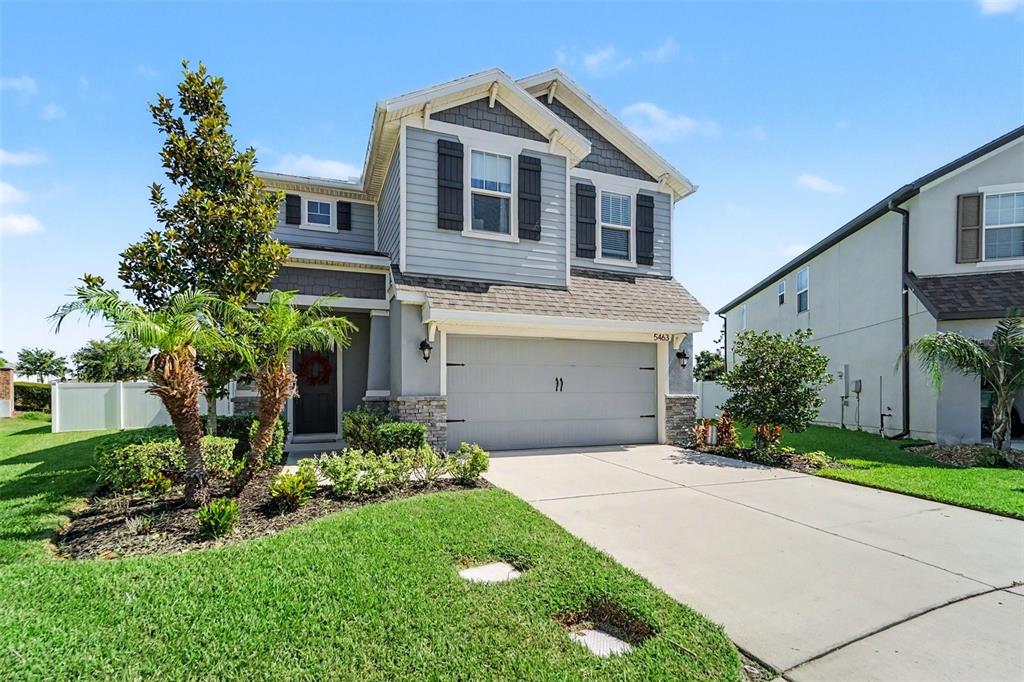 A two-story suburban house features light blue siding, a two-car garage, and a front lawn — 5463 LITTLE STREAM LANE, WESLEY CHAPEL, FL