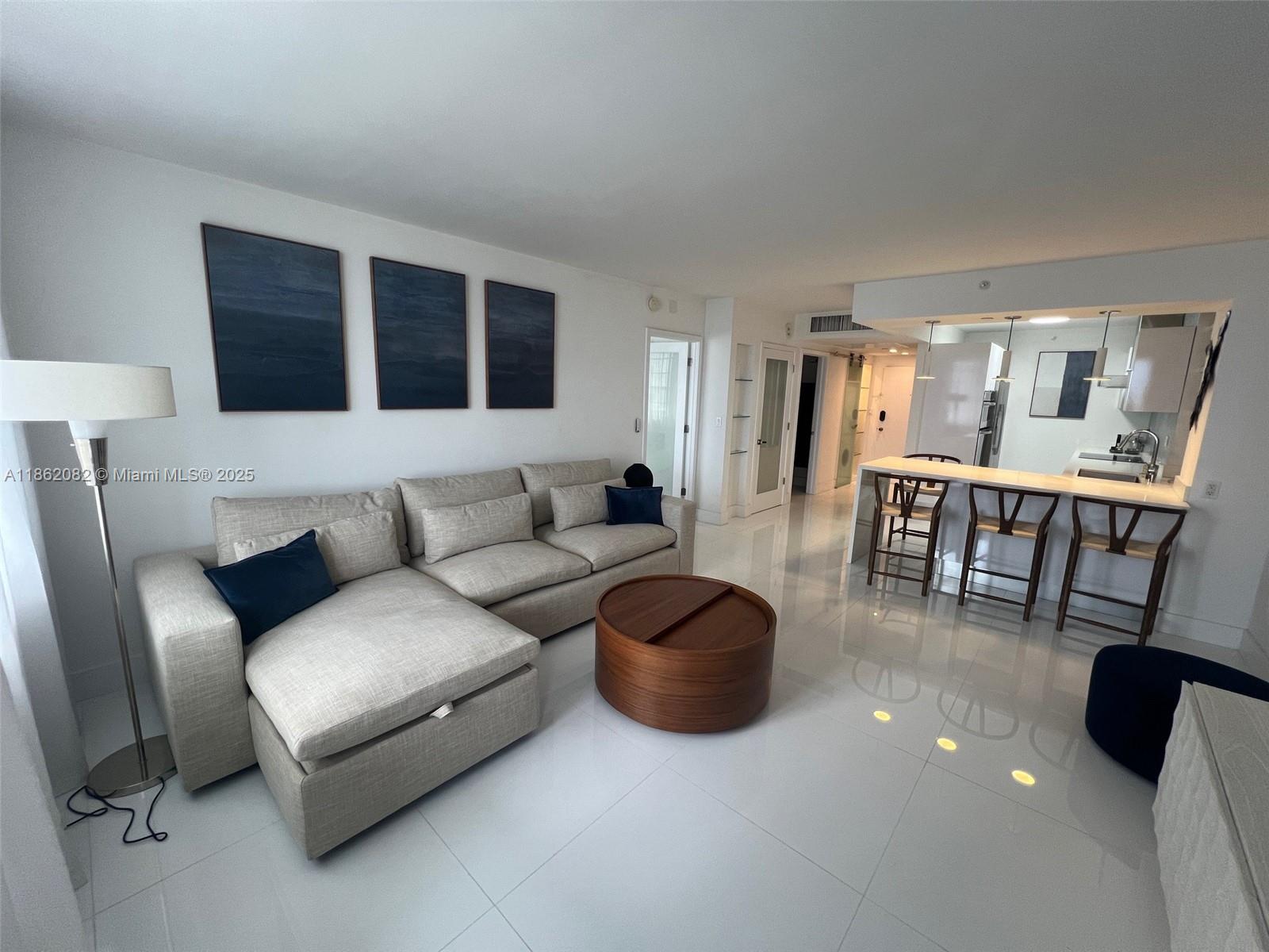 A modern living room features a sectional sofa, a round wooden coffee table, and a kitchen — 100 Lincoln Rd # 1022, Miami Beach FL 33139, MIAMI BEACH, FL