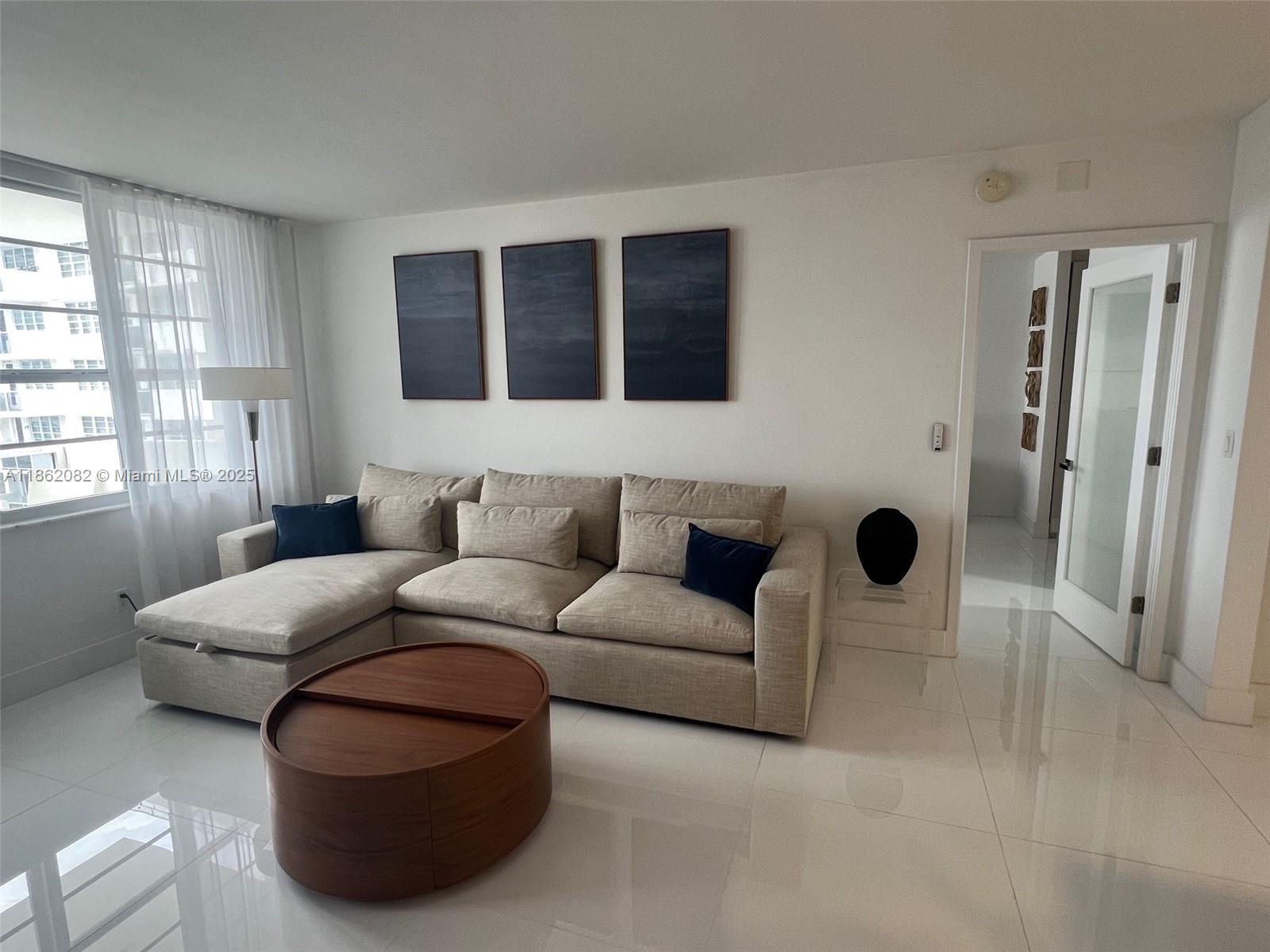 A living room features a beige sectional sofa, a round wooden coffee table, and white floors — 100 Lincoln Rd # 1022, Miami Beach FL 33139, MIAMI BEACH, FL