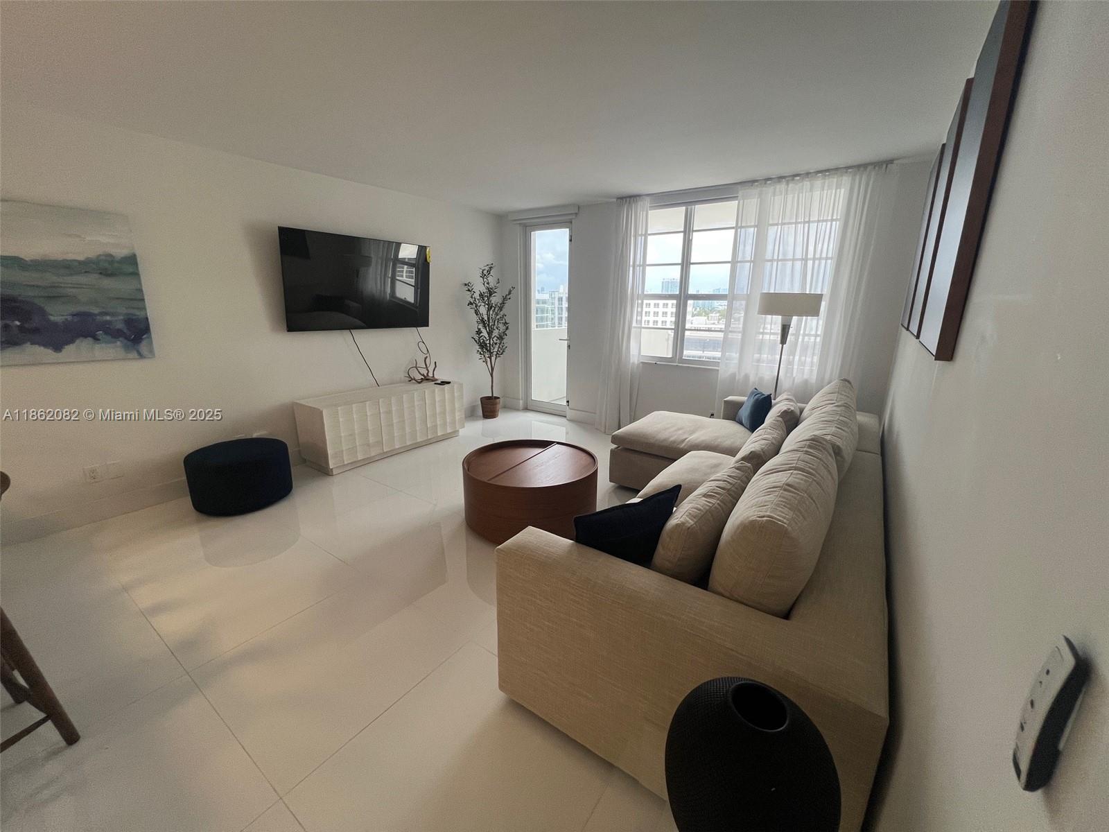 A modern living room features a beige sectional sofa, white tile floors, and a wall-mounted television — 100 Lincoln Rd # 1022, Miami Beach FL 33139, MIAMI BEACH, FL