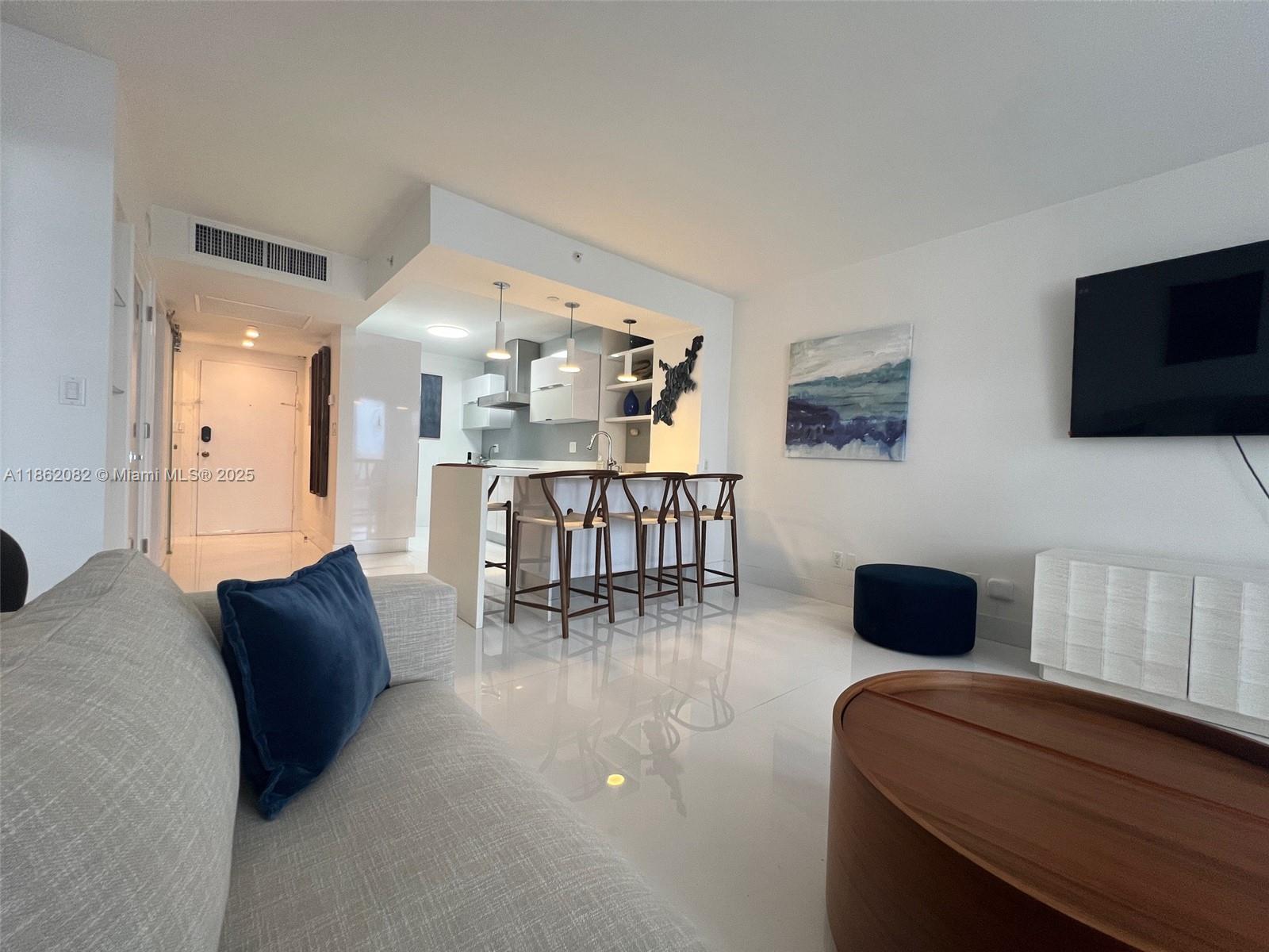 A modern living room with white tile floors, a kitchen island, and a mounted television — 100 Lincoln Rd # 1022, Miami Beach FL 33139, MIAMI BEACH, FL
