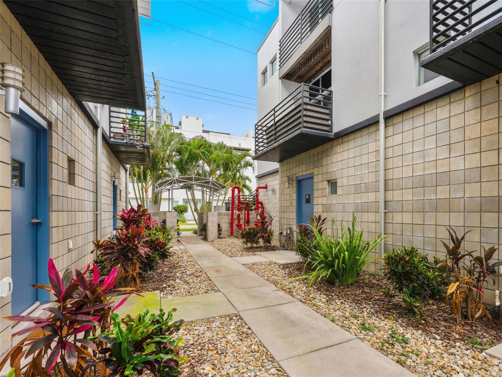 A concrete walkway leads between two multi-story buildings with blue doors and landscaping — 5008 S MACDILL AVENUE UNIT 16, TAMPA, FL