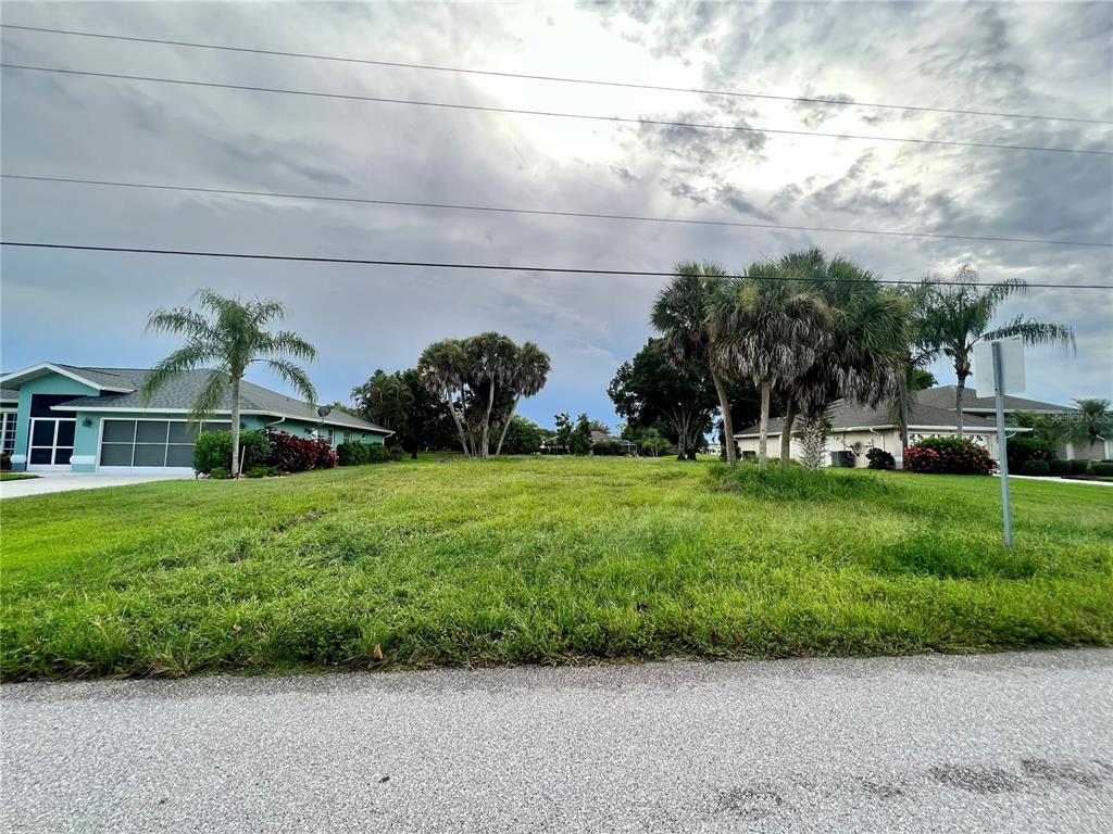 A vacant grassy residential lot sits between two existing houses under a cloudy sky — 11 SPORTSMAN ROAD, ROTONDA WEST, FL
