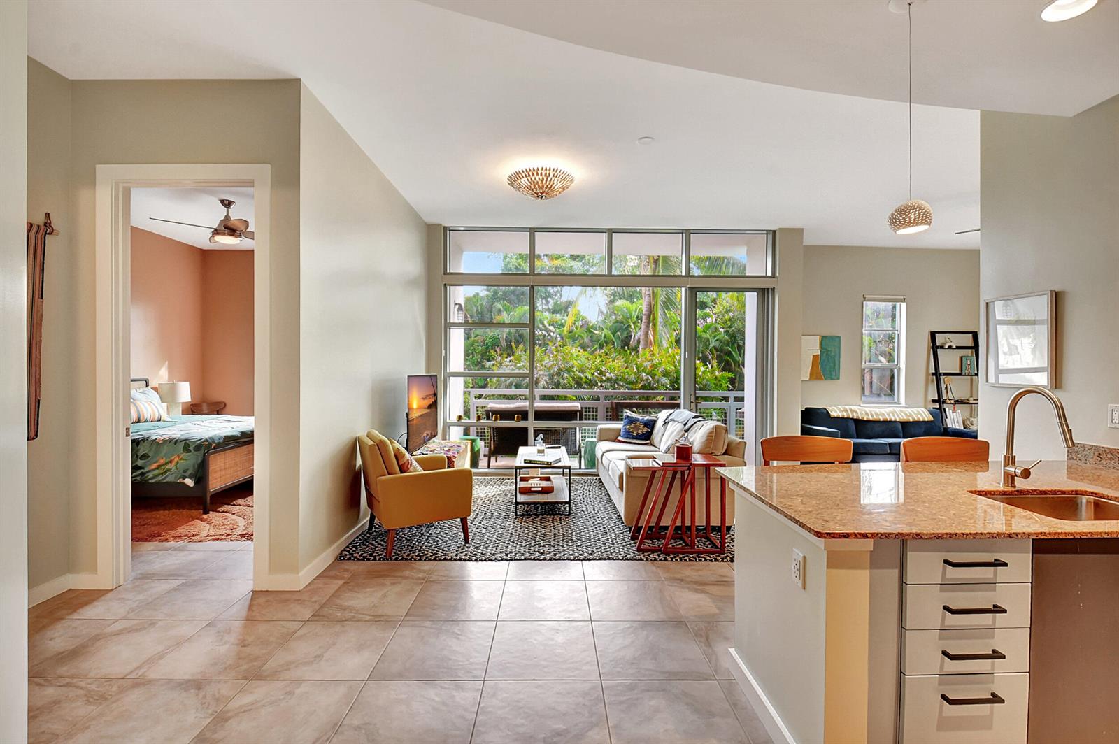 An open-concept living area features tile floors, a kitchen island, and a view of greenery — 365 SE 6th Avenue # 204, Delray Beach FL 33483, DELRAY BEACH, FL