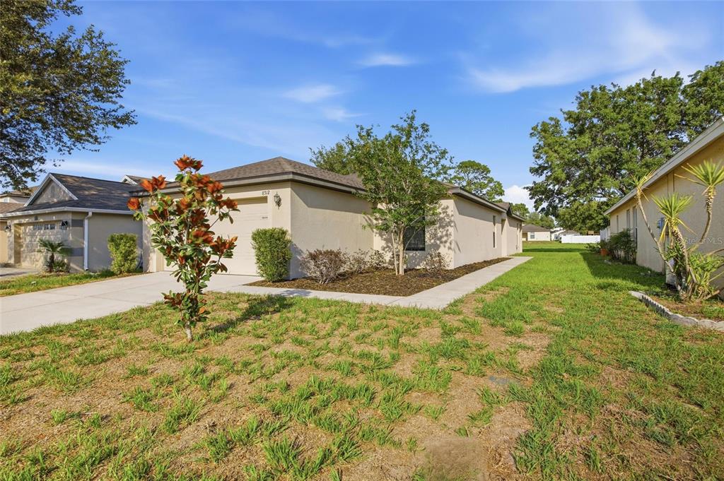 A single-story house with a beige stucco exterior, a concrete driveway, and a grassy yard — 8512 SILVERBELL LOOP, BROOKSVILLE, FL