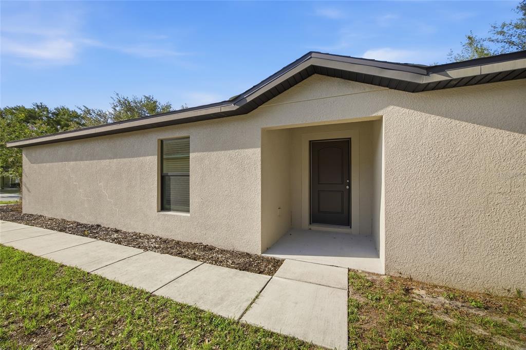 A beige stucco house exterior features a dark front door and a concrete walkway — 8512 SILVERBELL LOOP, BROOKSVILLE, FL