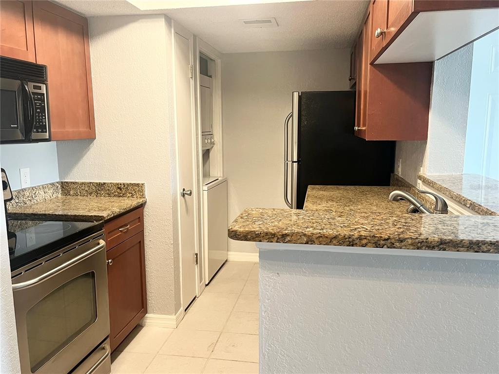 A kitchen features wood cabinets, granite countertops, stainless steel appliances, and an in-unit laundry closet — 10200 GANDY BOULEVARD N UNIT 813, ST PETERSBURG, FL