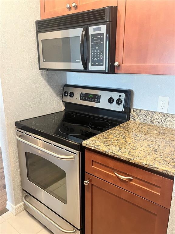 A kitchen features a stainless steel microwave, electric stove, and granite countertops with wooden cabinets — 10200 GANDY BOULEVARD N UNIT 813, ST PETERSBURG, FL