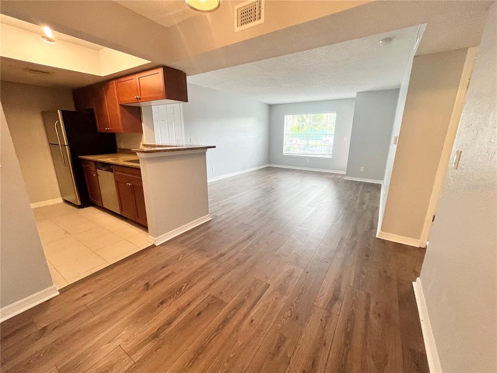 A kitchen with wood cabinets and a stainless steel refrigerator opens to a living area — 10200 GANDY BOULEVARD N UNIT 813, ST PETERSBURG, FL