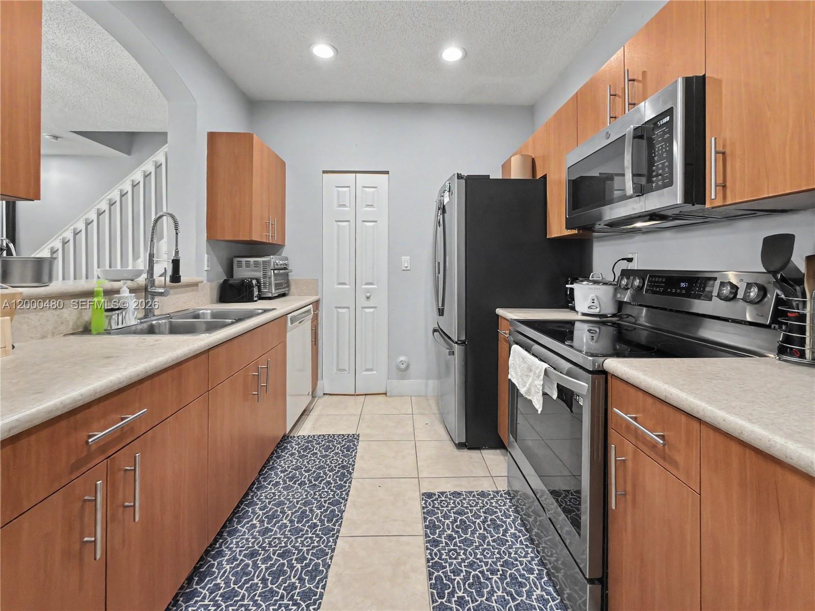 A kitchen features wood cabinets, stainless steel appliances, light countertops, and tile flooring — 1033 NE 42nd Pl, Homestead FL 33033, HOMESTEAD, FL
